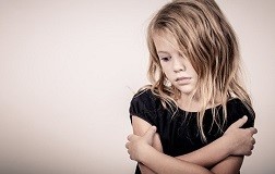 Portrait of sad blond little girl standing near wall