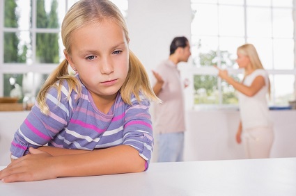 Little girl looking sad in front of fighting parents in the kitchen
